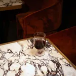 Hosteria Goblet 345ml in use, holding red wine on a white marble table with dark grey veining and a gold-trimmed edge.