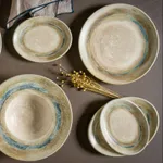 Overhead view of four Bonna Tranquil Round Coupe Plates in speckled cream glaze with earthy brown and turquoise blue rims.