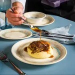 Bonna Tranquil Round Coupe Plate 230mm in use, cream ceramic with blue-green rim holding mashed potato and meat as gravy is poured.