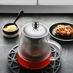 Brew Infusion Teapot With Vertical Stripes 600ml in use, filled with amber tea on a black trivet, featuring a ribbed glass body and steel lid.