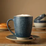 Grey Cast Espresso Saucer 125mm in use, holding a blue-grey mug and copper spoon on a wooden table.