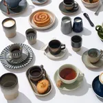 Overhead view of assorted stoneware tableware including the Tierra Brown Straight-Side Espresso 90ml cup and saucer in earthy tones