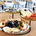 Chef Inox 3-tier seafood stand in use on a table, featuring brass trays with oysters, lobster, and prawns on ice.