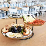 Chef Inox 3-tier brass and iron seafood stand in use, loaded with lobster, prawns, and oysters on a wooden table.