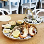 Chef Inox Round Seafood Stand 2-Tier Brass in use, holding a seafood platter on white ice stones in a restaurant setting.