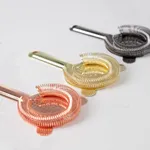 Close-up of three D-Still Hawthorn strainers in copper, gold, and stainless steel with coiled wire mesh baskets and engraved brand names.