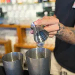 D-Still Multi Level Jigger 75ml Vintage Stainless Steel in use, held above mixing tins with etched measurement lines visible.