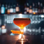Perception Wine coupe glass in use, filled with an amber cocktail and garnished with a curled orange peel on the rim