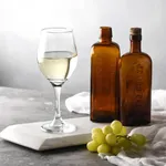 Perception Wine glass with white wine on marble, lifestyle shot with amber bottles and green grapes