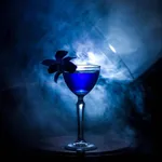 Libbey Nick and Nora glass in use, filled with a blue cocktail and garnished with a dark orchid on the rim
