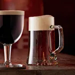 Bormioli Rocco Stern Beer Mug 510ml in use, filled with amber beer and foam on a wooden table next to a stemmed glass.