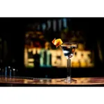 Libbey Modern America Nick & Nora glass in use on a wooden bar, filled with clear liquid and garnished with an orange peel.