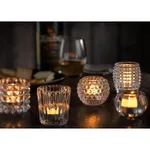 Utopia Ribbed Votive Clear in use, four lit holders with fluted, faceted, and beaded glass textures on a dark wooden table
