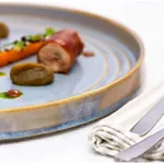 Urban Loft Azure Blue Sauce Dish close-up in use, holding prosciutto and vegetables, featuring a mottled blue-grey glaze and gold rim.