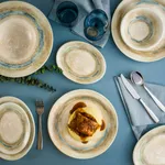 Bonna Tranquil Round Coupe Plate 270mm in use, cream ceramic with blue-green rim, set with food and cutlery.