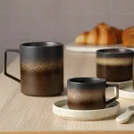 Tan Bark Straight-Side Mugs in use on a wooden table, showing matte speckled glaze and rectangular loop handles.