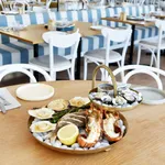 Chef Inox Round Seafood Stand 2-Tier Brass in use on a table with oysters, fish, and asparagus