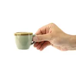 Olympia Kiln Moss Espresso Cup in use, held horizontally to show the sage-green ceramic body and tan rim band.