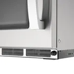 Close-up of the Apuro Heavy Duty Programmable Compact Microwave Oven's lower front corner, showing a white handle and silver base with ventilation grilles.