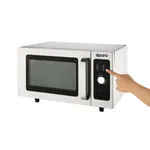 Apuro 25L commercial microwave in three-quarter view, stainless steel body, black glass door, hand pointing at manual rotary dial