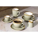 Olympia Kiln Moss ceramic cups and saucers in use, featuring a matte sage-green glaze, white interior, and raw brown rim.