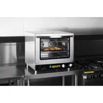 Apuro convection oven in use on a worktop, showing a tray of baked food inside and the black control panel with yellow logo.