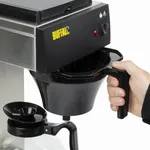 Close-up of the Apuro Manual Fill Pour-Over Filter Coffee Machine in use, showing a hand inserting a black filter basket into the stainless-steel brew head.