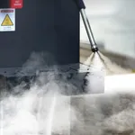 Benchstar Milk Frother Steamer in use, close-up of black body with red label and stainless steel wand spraying steam onto drip tray
