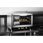 Apuro convection oven in use with door open, revealing croissants on a wire rack and two internal fans behind the black control panel.