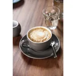 Olympia Cafe Cappuccino Cup Charcoal in use, filled with a latte featuring a heart-shaped foam design on a matching saucer.