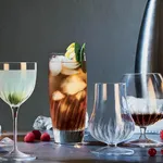 Luigi Bormioli Mixology Nick & Nora glasses in a lifestyle lineup, featuring a faceted highball with an amber cocktail and citrus garnish.