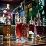 Close-up of five glass syrup dispensers with metal pour spouts, including an amber bottle embossed with No.3 ELIKIR and a crown.