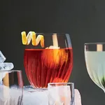 Close-up of the Luigi Bormioli Mixology Nick & Nora 150ml glass filled with a reddish-orange cocktail and a spiralled citrus peel garnish.