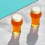 Pasabahce 285ml tin can cocktail glasses in use, filled with amber beer and topped with a white head on a silver surface.