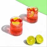 Pasabahce 285ml tin can glasses in use, filled with red cocktails and garnished with fruit, featuring a ribbed lower texture.