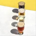 Overhead view of four Pasabahce 285ml tin can glasses filled with various beers, showing their tulip shape and footed stems.