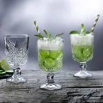 Pasabahce Timeless Nick & Nora glasses in use, showing cut-crystal bowls with green cocktails, mint, and striped straws.