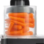 Dito Sama vegetable slicer in use, showing the transparent bowl filled with carrots and black pusher cap on the base.