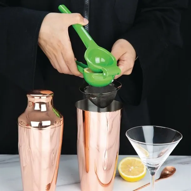 Green Olympia Hand Lime Squeezer in use, side view, pressing a lime over a copper shaker
