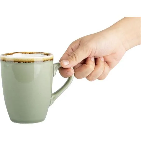 Olympia Kiln Moss Mug in use, held by a hand, showing the glossy sage-green ceramic surface and frothy coffee inside.