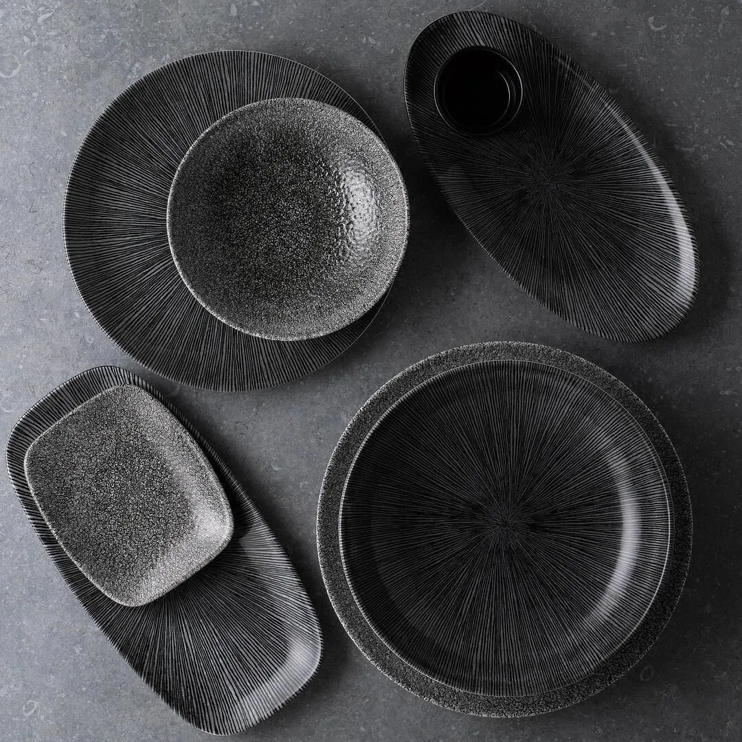 Churchill Round Coupe Bowl in black ceramic with speckled interior and ribbed exterior, shown in an overhead flat-lay with matching tableware.