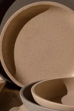 Luzerne Share Bowl close-up showing speckled matte beige interior and wide rim, nested with grey plate on textured fabric.