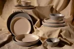 Luzerne 256mm share bowl in speckled cream and grey ceramic, displayed in a stacked arrangement on beige fabric.