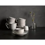 Matte white ceramic teacups with C-shaped handles, shown in a lifestyle arrangement with one cup on a saucer and others stacked.