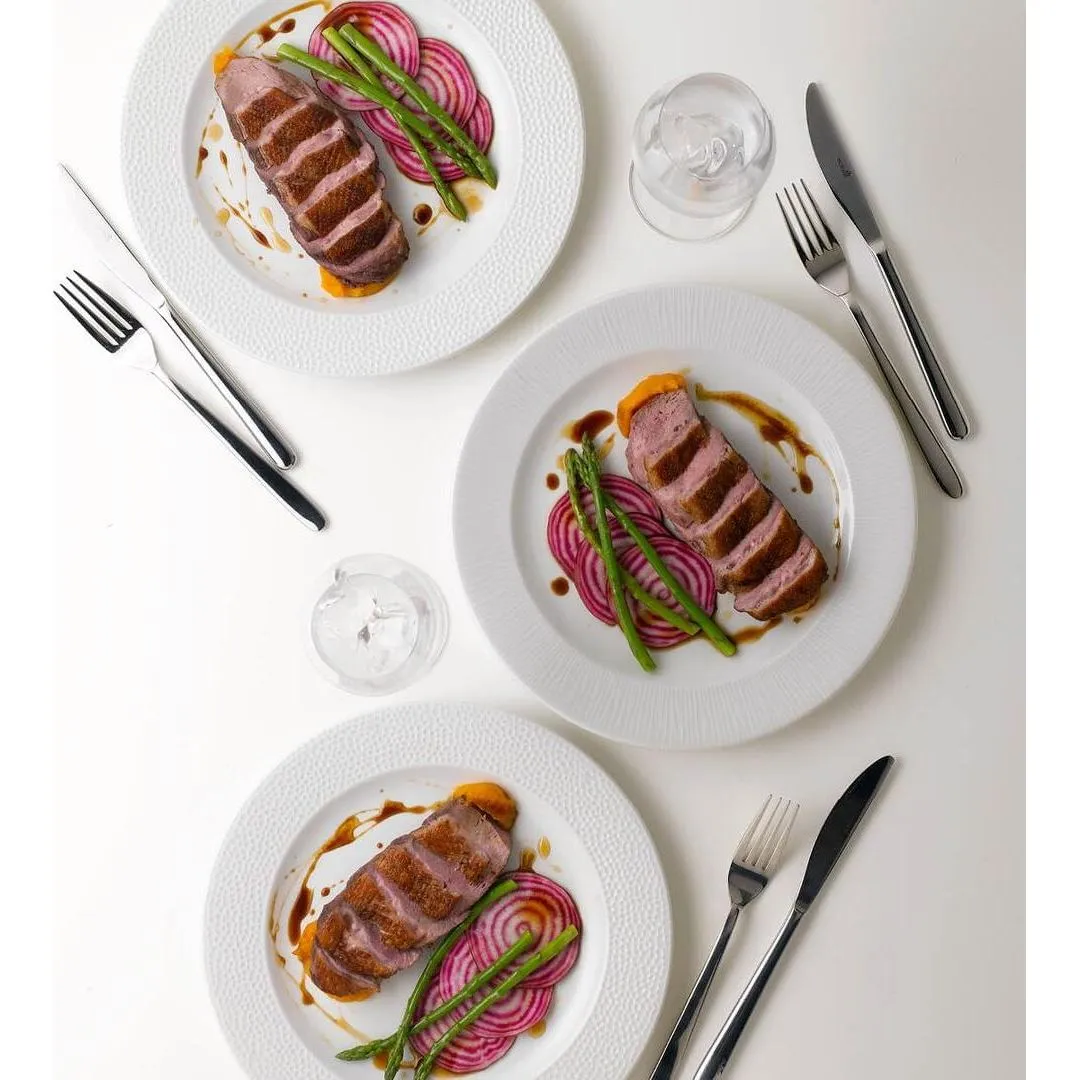 Churchill Round Wide Rim Plate in use, overhead view of three white plates with textured rims holding plated meat and vegetable dishes.