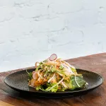 Luzerne Round Bowl in use, filled with mixed salad, showing its wide, shallow profile and matte black finish.