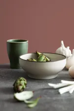 Luzerne Round Bowl in Dusted White, low side angle in use, filled with artichokes, featuring a matte off-white exterior and dark rim.