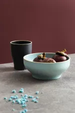 Luzerne frosted blue round bowl in use, filled with mangosteens on a stone surface