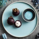 Luzerne Frosted Blue Share Bowl top-down view holding mangosteens and blue sugar on a grey surface
