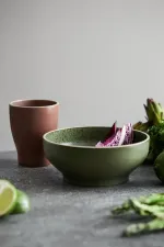 Luzerne Smokey Basil round bowl in use, filled with sliced red onion, showing matte sage exterior and speckled green interior glaze.